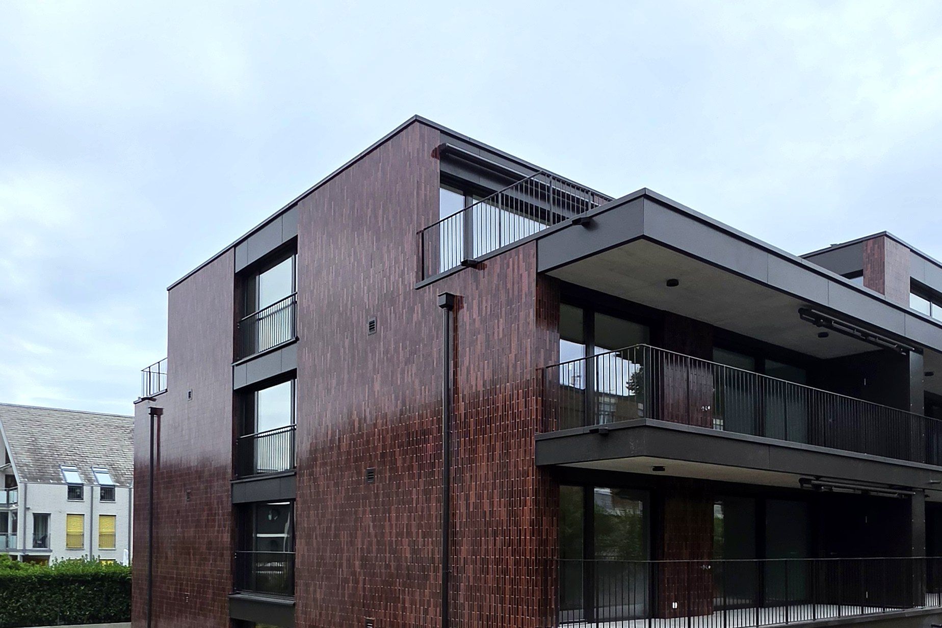 Mehrfamilienhaus mit dunkelroter Klinkerfassade und durchlaufenden Balkonen