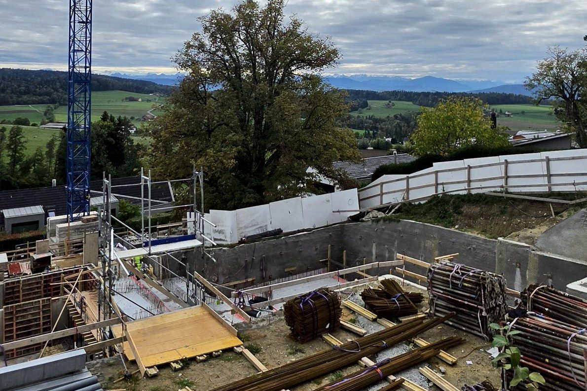 Shell in the excavation with rebar, crane, an old lime tree and Alpine panorama behind