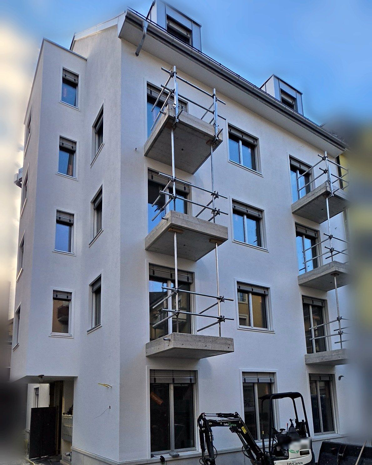 White facade with concrete balconies, fall protection still fitted; surroundings blurred