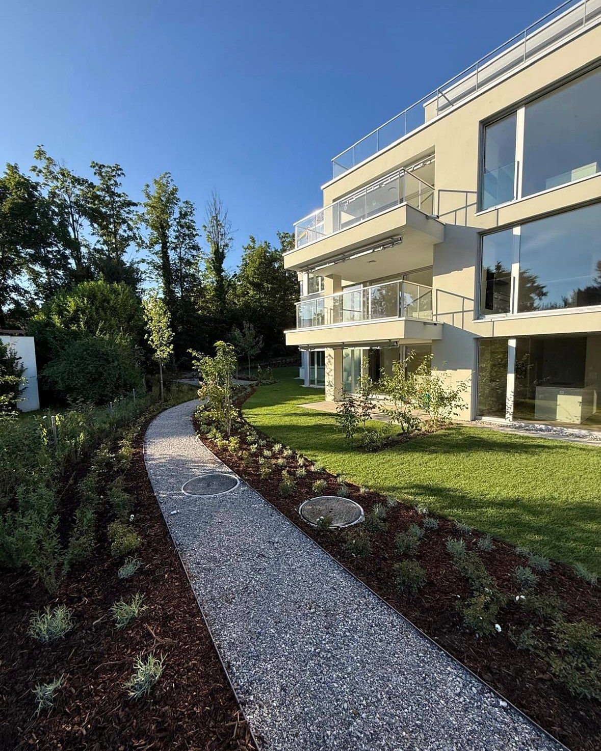 Mehrfamilienhaus mit Balkonen, davor Kiesweg und neu bepflanzte Umgebung