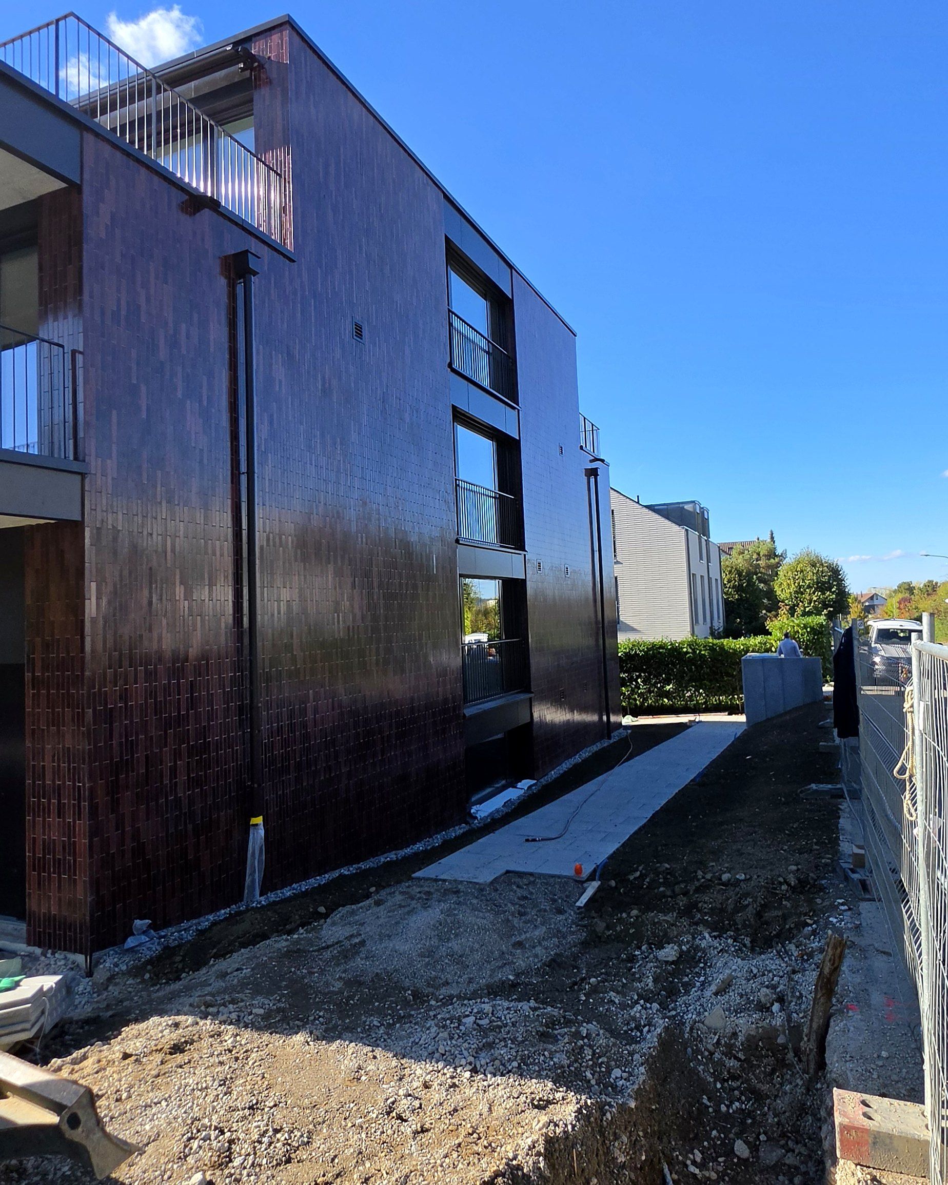 Seitenfassade mit dunkelroter Klinkerverkleidung, davor laufende Umgebungsarbeiten