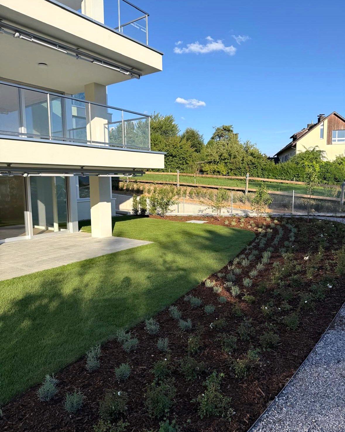 Gartensitzplatz unter den Balkonen, frischer Rasen und Bepflanzung