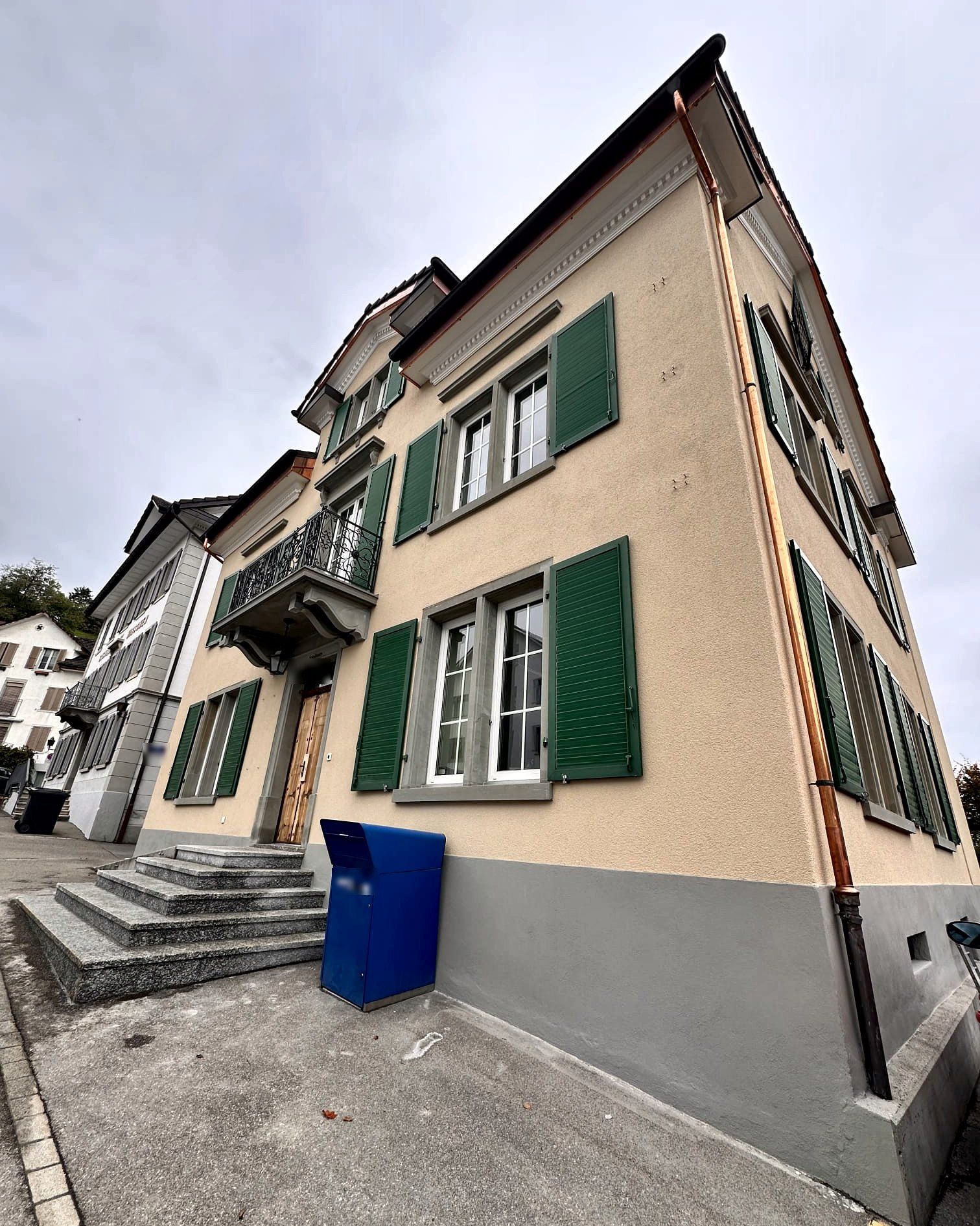 Hausecke mit Treppe, Balkon und Kupferablauf, Schrift unkenntlich gemacht