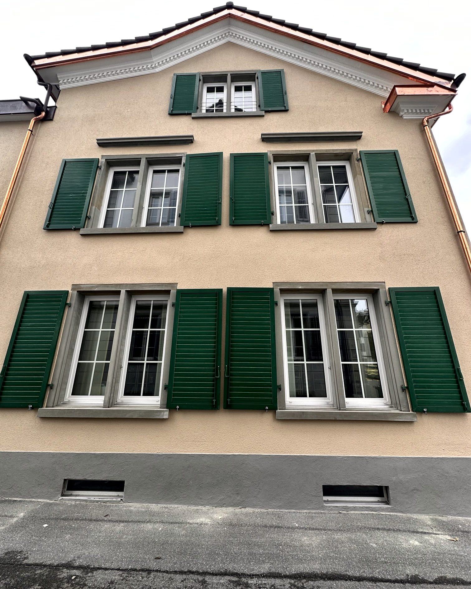 Giebelfassade mit grünen Läden und grauem Sockel