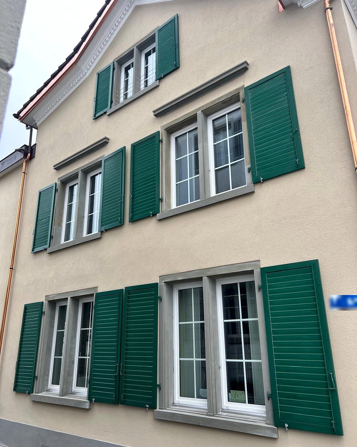 Seitenfassade mit Jalousieläden und Kupferablauf, Strassenschild unkenntlich gemacht