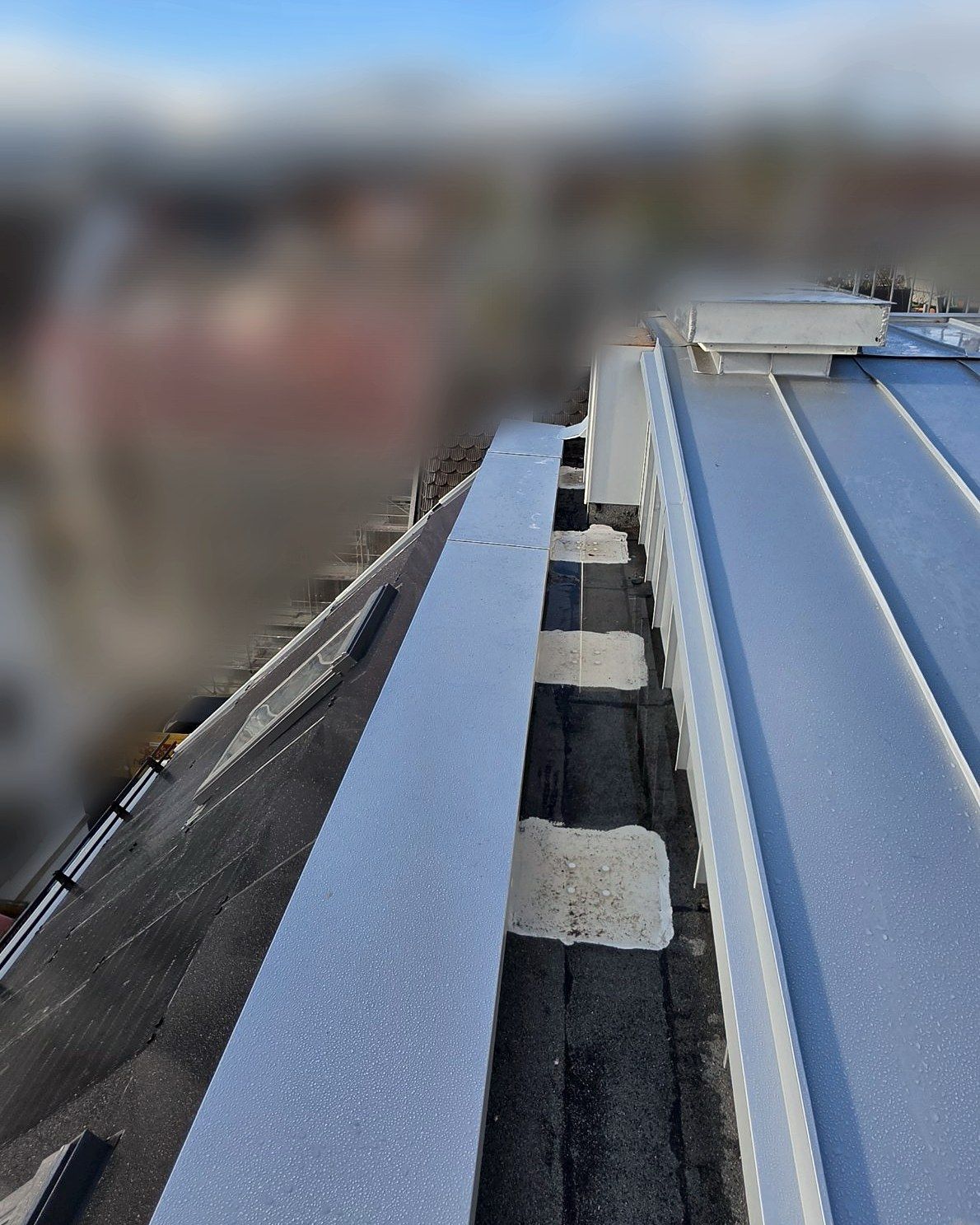 New metal coping on the parapet, the city blurred behind