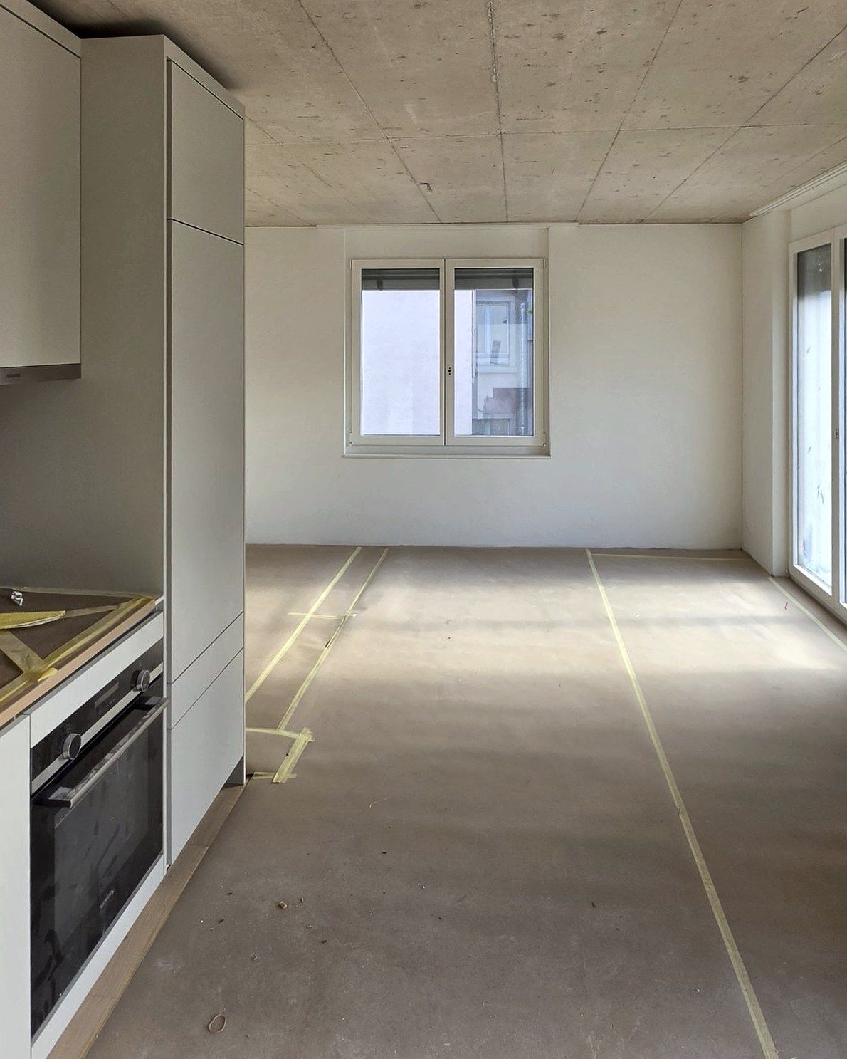 Living room with fair-faced concrete ceiling, kitchen and covered floor