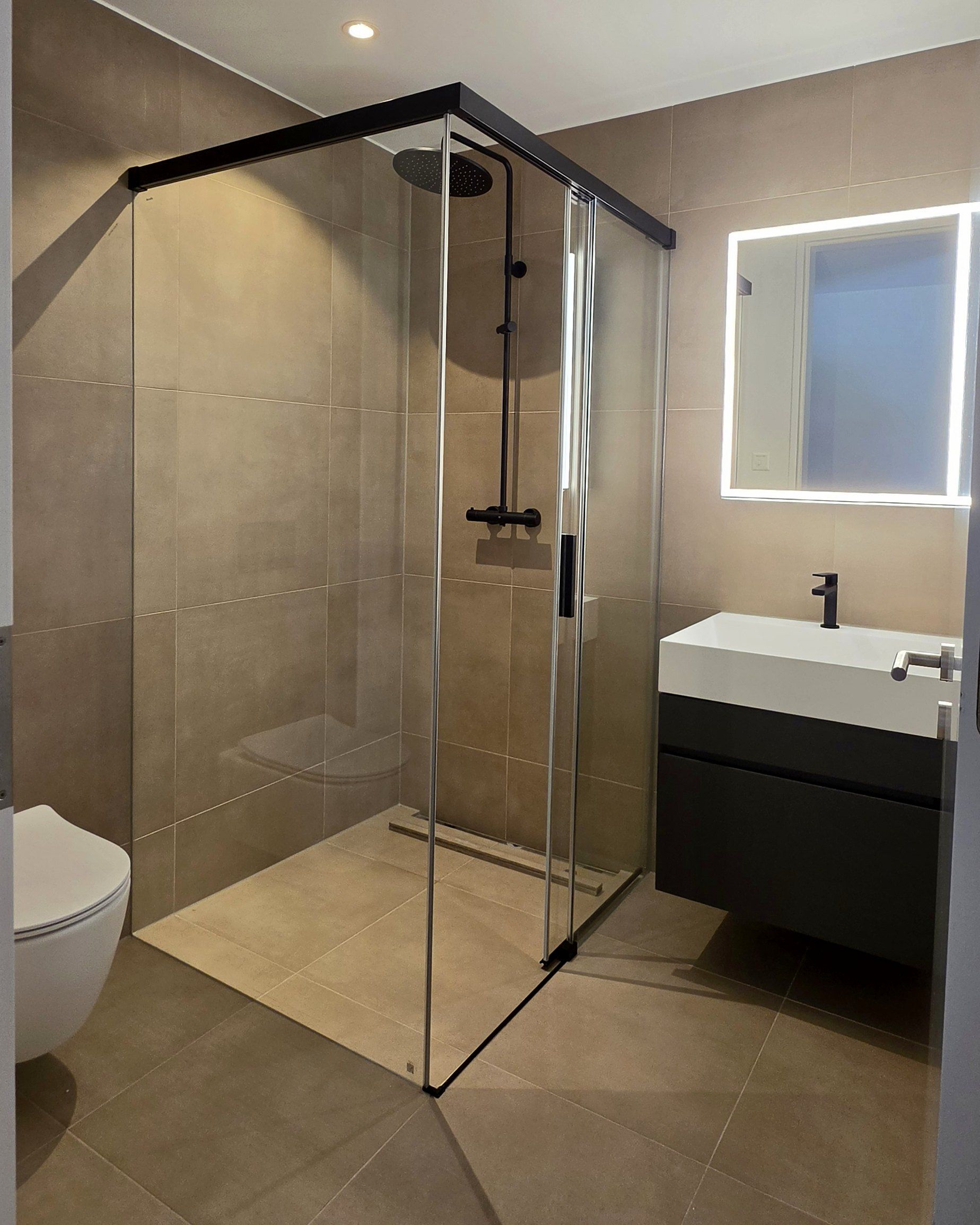 Dusche mit Glasabtrennung und beleuchtetem Spiegel