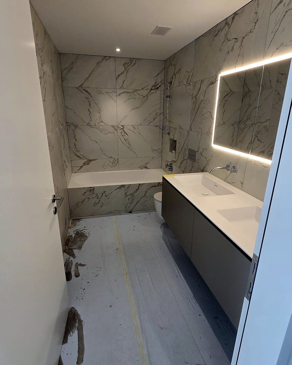 Bad mit Wanne, Wandplatten in Marmoroptik und beleuchtetem Spiegel