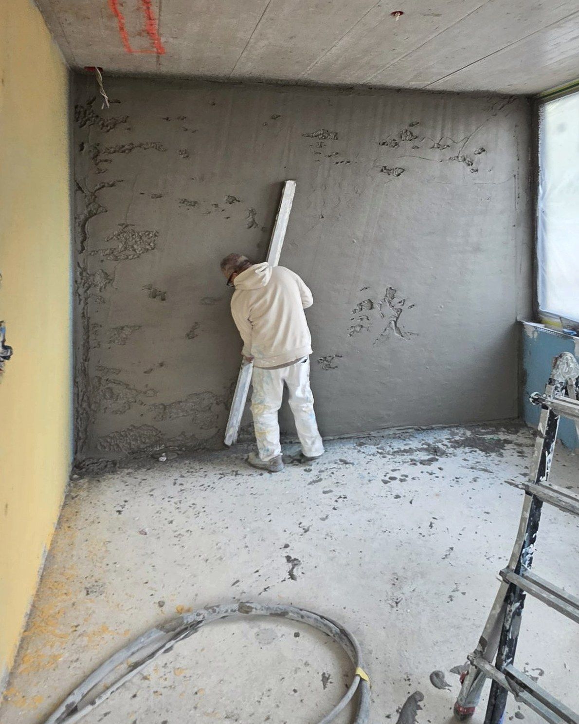 Gipser zieht den Grundputz an einer Wand ab, Sichtbetondecke